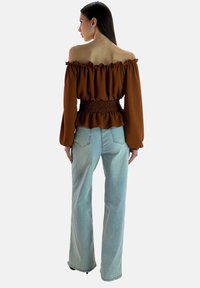 Brązowa bluzka z odkrytymi ramionami z falbankami na krawędziach i marszczoną talią; zestawiona z jasnoniebieskimi dzwonowymi dżinsami, z efektem wyblakłym i kieszeniami.