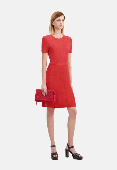 Robe tricot rouge avec un motif texturé et des manches courtes, accompagnée d'une pochette matelassée rouge et de sandales à plateforme noires.