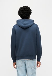 Μπλε σκούφο φούτερ με ευρύχωρο κουκούλι, ριμπ μανσέτες και τελείωμα. Διαθέτει απαλή υφή και άνετη γραμμή, εμφανιζόμενο από πίσω.