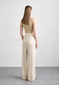 Un débardeur beige à côtes associé à un pantalon large en maille léger et aéré. Texture lisse et coupe ample, mettant en avant un style décontracté et confortable.
