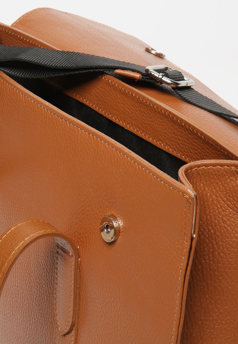 Sac en cuir marron avec une finition texturée, doté d'une bandoulière noire et d'une fermeture à bouton-pression magnétique. L'intérieur est doublé de tissu noir.