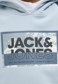 Svijetloljubičasti dukserica s grafičkim printom u tamnoplavoj boji s natpisom "JACK & JONES." Uključuje horizontalne pruge i teksturirane detalje.