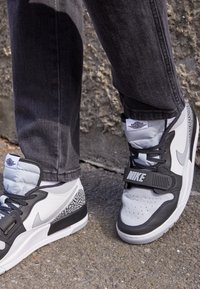 Tenisky Nike s kombinací šedé a bílé kůže, texturovanými akcenty, polstrovaným límcem a výrazným páskem s brandingem "NIKE".