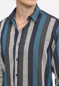 Button-up shirt featuring vertical stripes in teal, gray, and navy. Material appears lightweight with a textured finish. Small button details visible.