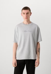 Gray cotton T-shirt with a relaxed fit and short sleeves, featuring embroidered "Calvin Klein" logo on the chest. Simple design, soft texture.