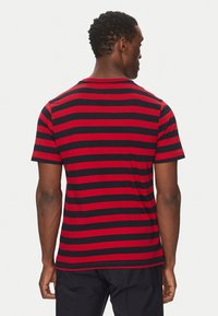 T-shirt a strisce rosse e nere, maniche corte, in cotone, colletto tondo, con un design aderente e una texture liscia.