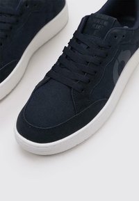 Baskets bleu marine avec un mélange de daim et de toile, dotées d'une semelle en caoutchouc blanche, d'un bout rond et de lacets plats. Détail de logo subtil.