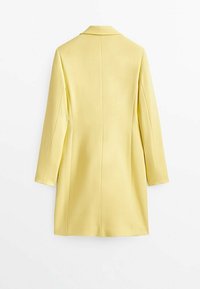 Long manteau jaune à manches longues et col, vu de dos sur fond blanc.