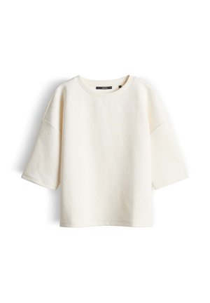 Crèmekleurig topje met korte mouwen, voorzien van een subtiel reliëf met bloemenpatroon en een ronde halslijn, weergegeven op een witte achtergrond.