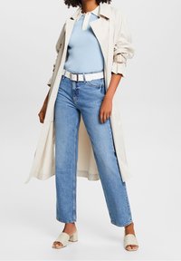 Trench beige claro sobre una camiseta azul de canalé, combinado con jeans de tiro alto en un azul claro y sandalias de tacón bloque beige.