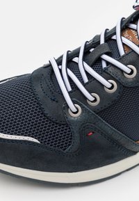 Marinblå sneakers med mesh- och mocka-texturer, vita snören genom metallögon, och röd accentstitching nära sulan.