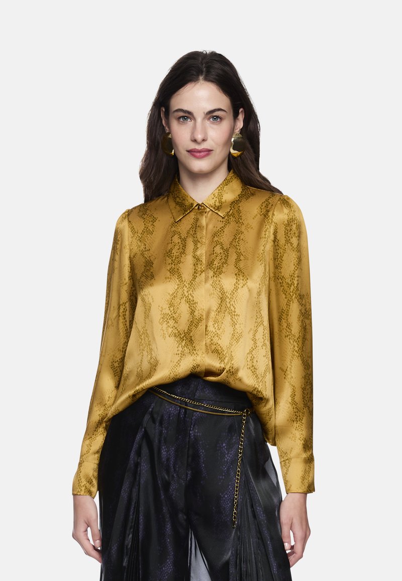 Mustard yellow blouse with a snake print pattern, satin texture, button-down collar, and long sleeves, paired with black pleated pants.