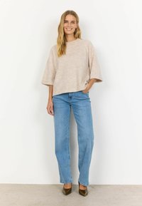 Maglione beige, con texture, a maniche corte abbinato a jeans in denim azzurro chiaro a vita alta e tacchi a punta marroni. Design minimalista.