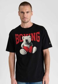 Camiseta de algodón negra con un gráfico de un oso de peluche con guantes de boxeo rojos, con la palabra "BOXEO" impresa en letras rojas en negrita arriba.