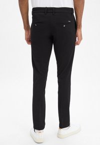 Pantalons noirs à coupe slim, dotés de deux poches arrière avec boutons, de passants de ceinture et d'une texture de tissu lisse. Associés à des baskets blanches.