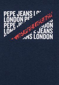 Námořnické tričko s bílým a červeným textem "PEPE JEANS LONDON." Obsahuje diagonální červené a bílé designové prvky. Měkká, texturovaná tkanina.