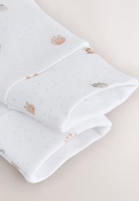 Närbild av vita babypyjamas ärmar med små djuransikten och mönster av ljusgrå prickar.