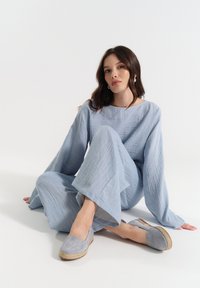 Jasnoniebieski, teksturowany zestaw wypoczynkowy z długimi rękawami i szerokimi spodniami, połączony z szarymi espadrylami na wsuwkę. Prosty, swobodny design.