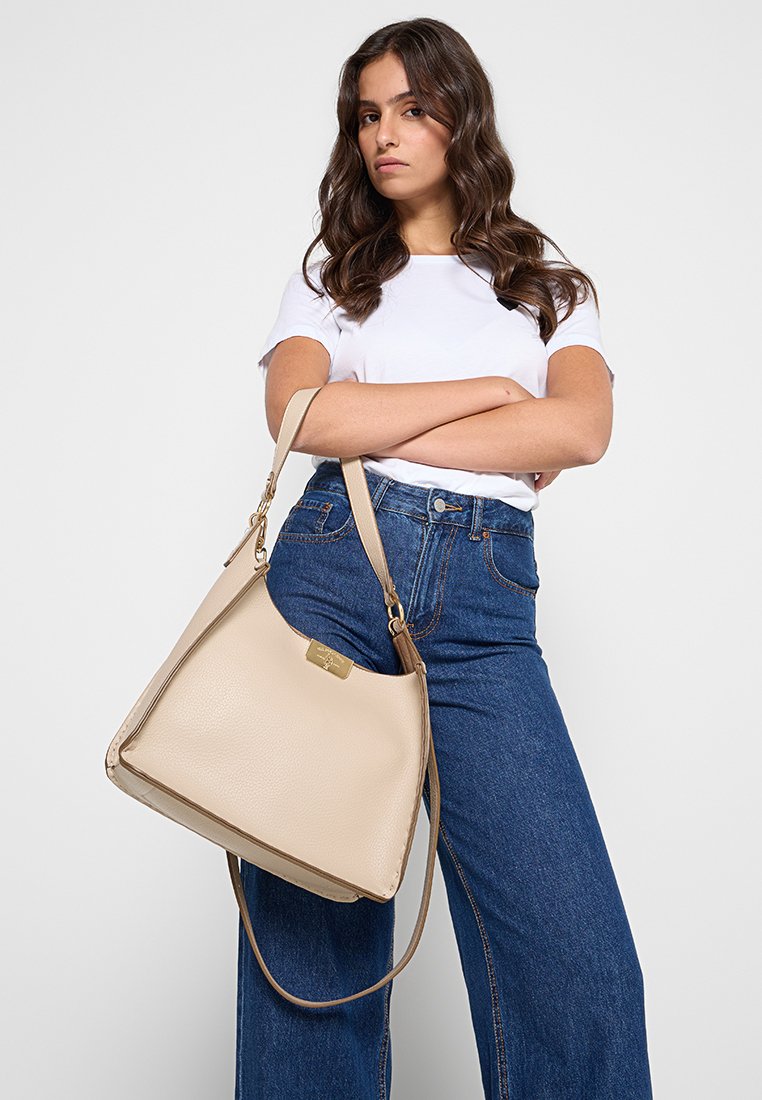 Borsa a mano in pelle beige con forma strutturata, dotata di un ampio scomparto principale e tracolla regolabile, su uno sfondo grigio.