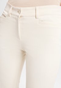Crèmekleurige, slanke broek met een rits- en knoopsluiting; heeft twee voorkanten zakken en een gladde, gestructureerde stof.