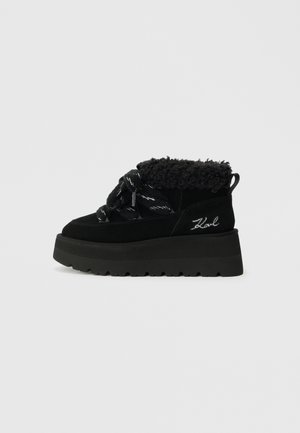 Botas de tornozelo em nubuck preto com um colarinho de pelúcia sintética, sola de plataforma espessa e atacadores com padrão. Costura detalhada e logo na lateral.