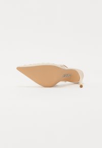 Pointed-toe stiletto heel in beige with a smooth upper and a textured, light brown sole. Features subtle decorative accents along the edge.
