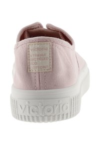 Ljusrosa tygsko med texturerad yta, vit gummisula och en rektangulär etikett med varumärkesdetaljer på hälen.