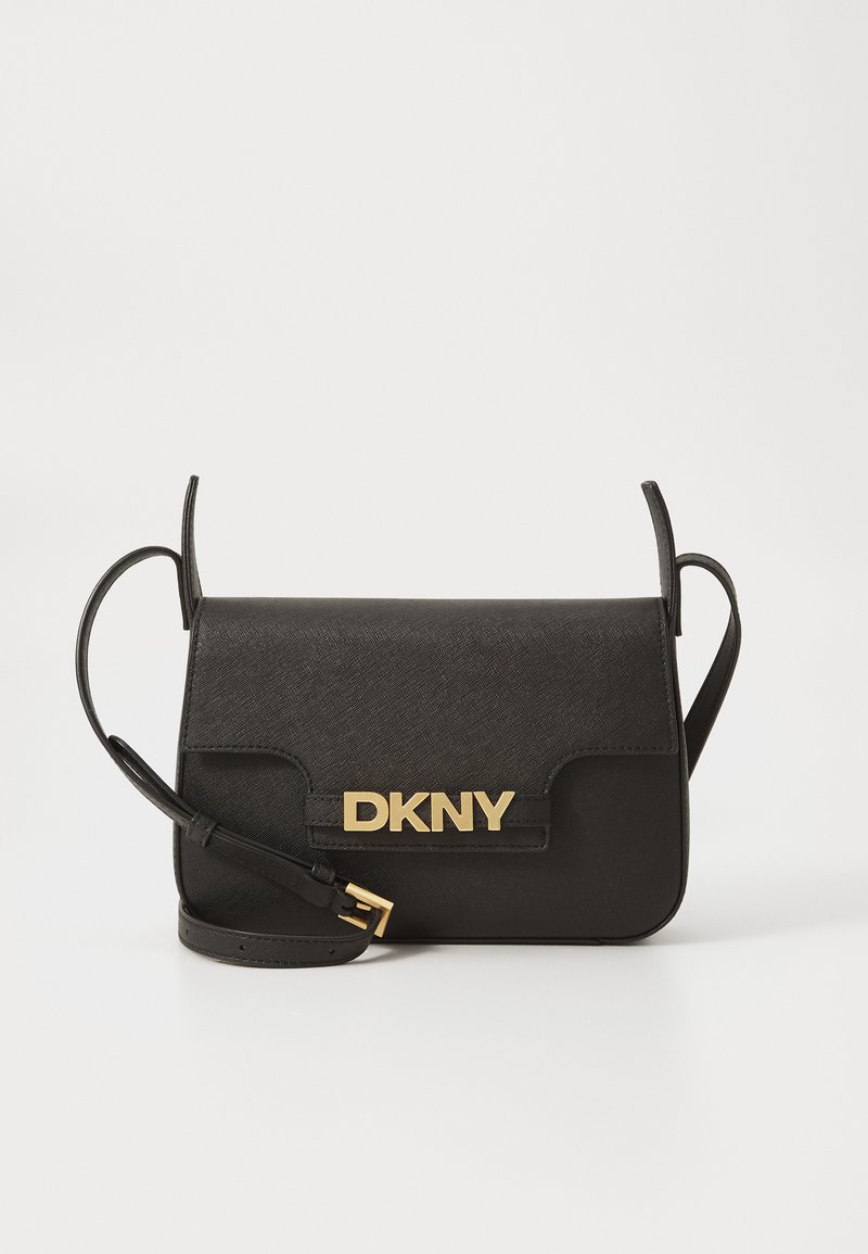 Juoda DKNY per petį nešama tašė, pagaminta iš tekstūruotos medžiagos, su auksiniu logotipu, užsegimu ant dangtelio ir reguliuojamu diržu. Minimalistinės stačiakampio formos.
