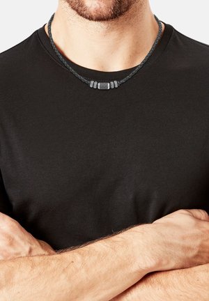 Maglietta nera a maniche corte indossata da una persona. È visibile una collana intrecciata con una perla centrale grigia e tre perle argentate decorative.