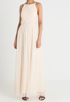 Nainen pukeutunut hihattomaan, lattiaan ulottuvaan vaaleanpunaiseen mekkoon, jossa on pitsikoristelu vyötäröllä ja laskostettu yläosa, yhdistettynä mustiin avokkaisiin.