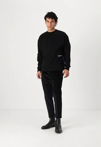 Svart sweatshirt med rund hals, långa ärmar och en liten loggdetalj fram. Kombinerad med smala svarta byxor och svarta ankelstövlar.