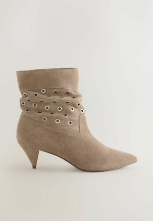 Bež gležnjar iz antilopa z ostro konico, tanko peto in nabranim dizajnom z okraski iz kovinskih obročev na strani.