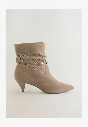 Bež gležnjar iz antilopa z ostro konico, tanko peto in nabranim dizajnom z okraski iz kovinskih obročev na strani.