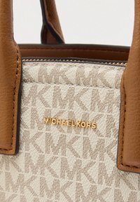 Bolso blanco con un logo MK estampado, detalles de cuero marrón y herrajes dorados. Costuras detalladas y forma estructurada.