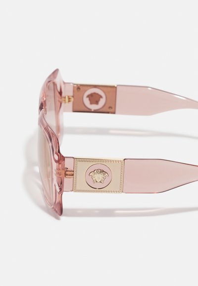 Óculos de sol cor-de-rosa translúcidos com um detalhe em dourado, apresentando o logótipo da Medusa nas hastes e um design de armação esculpido.