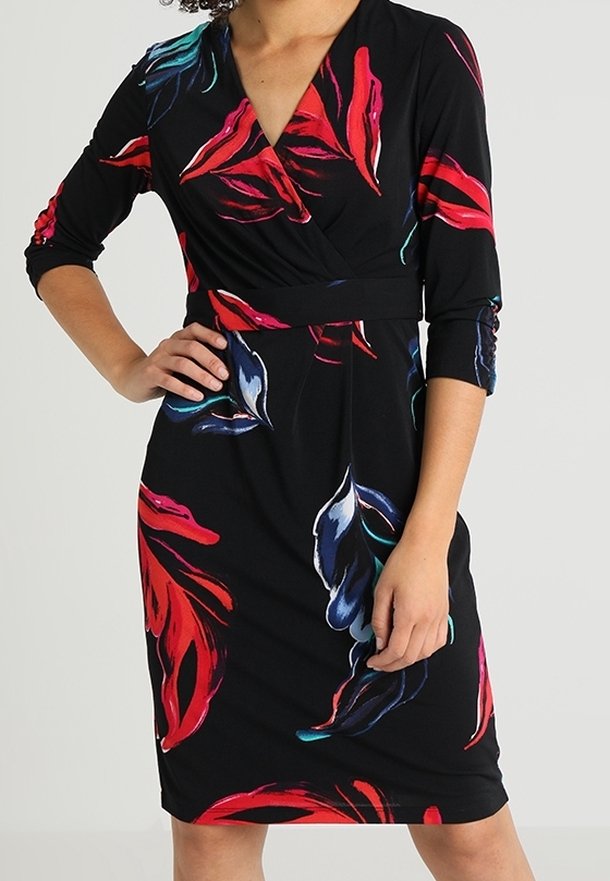 Femme portant une robe noire à motifs floraux rouges et bleus, manches trois-quarts et corsage style cache-cœur.