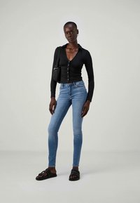 Fekete, hosszú ujjú felső gomb részletekkel, világoskék skinny farmerral és fekete csúsztatós szandállal. A fazon testhez simuló, sima textúrával.