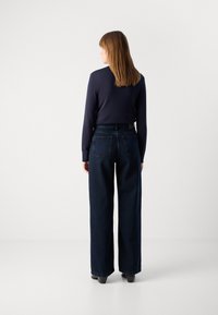 Wijde donkere spijkerbroek met zijzakken en achterzakken, gecombineerd met een passend langwerpig navy shirt. Soepele textuur, casual ontwerp.