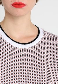 Pletený svetr s texturovaným vzorem v růžové a černé barvě, s černobílým žebrovaným kulatým výstřihem. Detailní pohled na límec a látku.