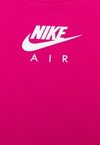 Světle růžový nátělník s žebrovanou strukturou a bílým logem "NIKE" nad textem "AIR". Čistý, moderní design ideální pro sportovní oblečení.