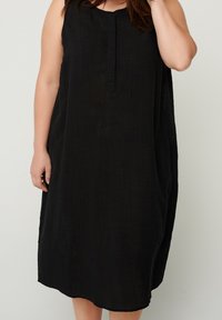 Černé bezramínkové šaty z texturované látky, se zaobleným výstřihem a volným střihem, který sahá těsně nad kolena.
