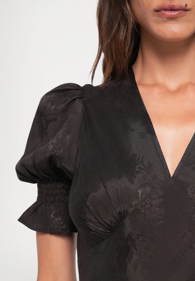 Zwarte jurk met een diepe V-hals, pofmouwen en een gestructureerd bloemenpatroon. Kenmerkt zich door smockdetails aan de zoom van de mouwen en de lijfjes.