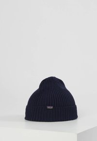 Mornarska pletena kapa z rebrasto teksturo in ovitkom. Ima majhno logotip oznako na strani. Narejena iz mehkega, raztegljivega materiala.