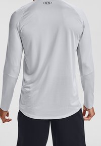 Takaa päin otettu kuva henkilöstä, joka pukeutuu vaaleanharmaaseen pitkähihaiseen urheilupaitaan, jossa on pieni musta logo yläselässä, ja mustiin shortseihin.