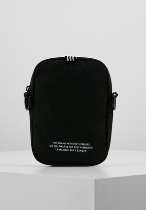 Sac bandoulière rectangulaire noir avec trois bandes blanches sur le dessus et marquage textuel blanc en anglais, allemand et français à l'avant.