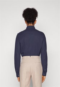 Camisa de manga larga azul marino con puños de botón, ajuste entallado. Pantalones en tono beige claro con una textura suave y dos bolsillos traseros. Sin patrones visibles.