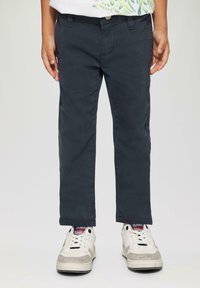 Dunkelblaue Kinderhose aus Baumwolle mit geradem Schnitt und Taschen, kombiniert mit weißen Sportschuhen mit grauen Akzenten.