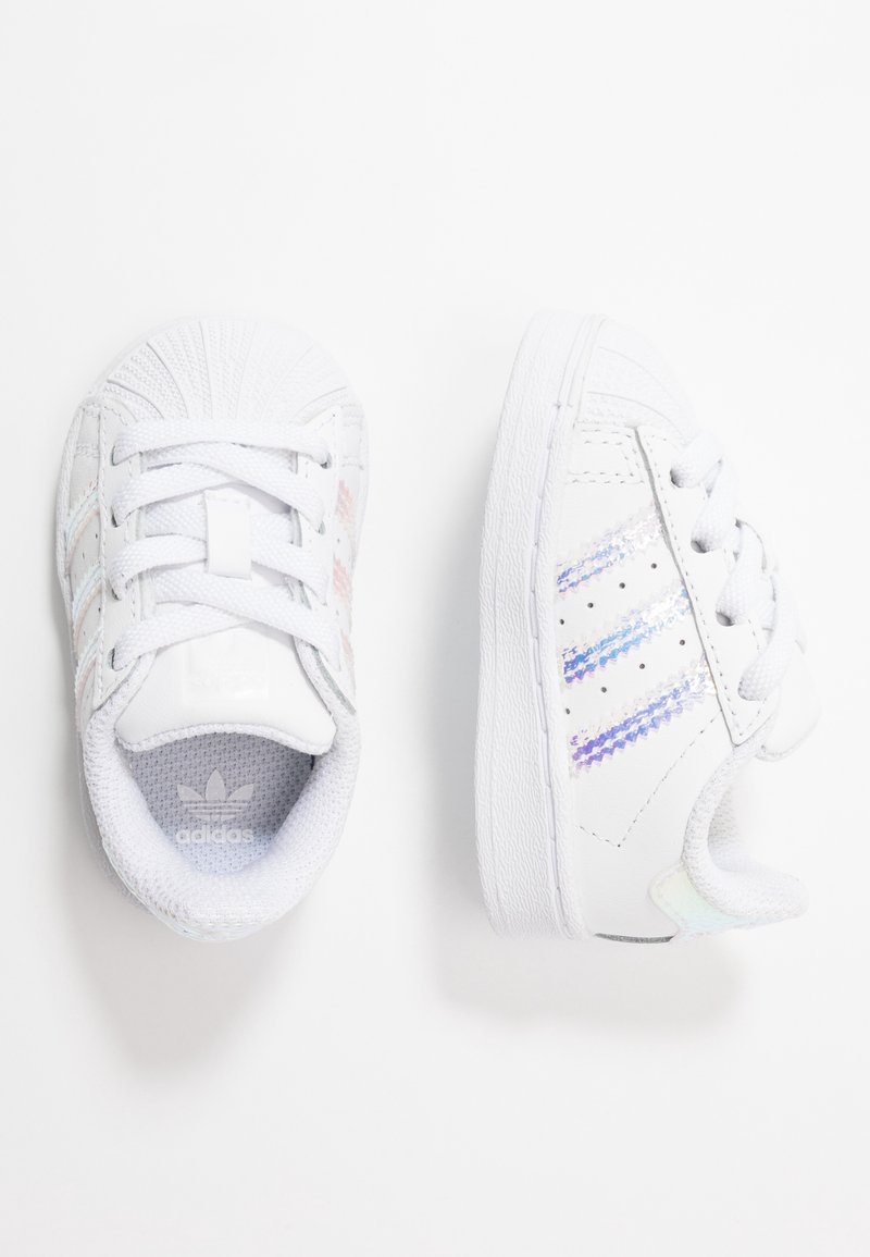 Valkoiset lasten tennarit, joissa on kuvioitu kumipohja, nyöritys ja helmiäisraidat sekä klassinen kuorikärki.