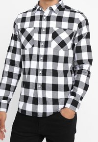 Zwart-wit geruit flannel overhemd met een boord met knoopsluiting, lange mouwen en twee borstzakken. De stof lijkt zacht en textuurrijk.