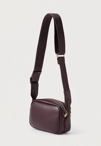 Καφέ δερμάτινη τσάντα χιαστί σε ορθογώνιο σχήμα, με χρυσή φερμουάρ και ρυθμιζόμενο λουρί που διαθέτει ανάγλυφο λογότυπο. Λείο υλικό.